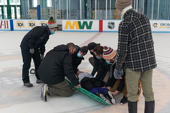 Photo of MSAT students wearing masks on an ice rink, helping an injured hockey player who is laying on the ice