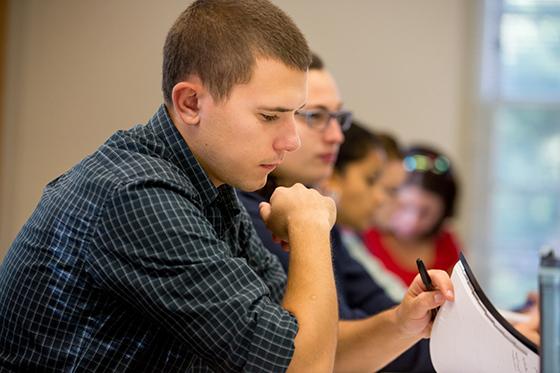 Photo of a male Chatham University student leafing through a pamphlet at a lecture hall desk. 