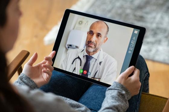 Photo of a patient holding a tablet with a video call open, speaking to a medical professional.