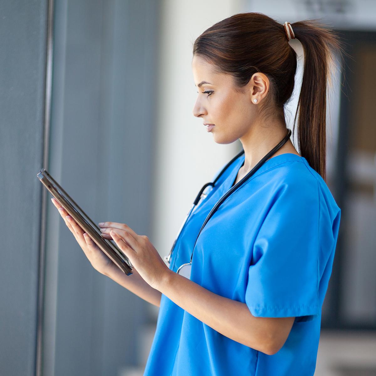 Photo of a woman nurse in blue scrubs reading a tablet