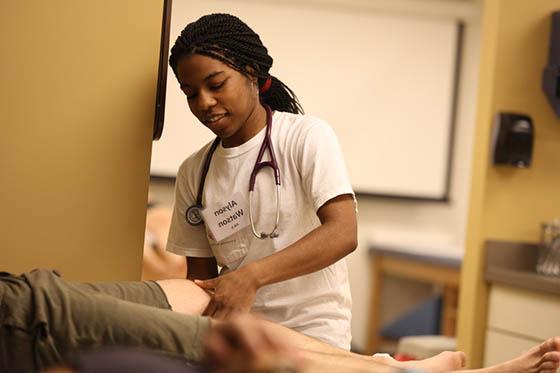 Photo of a Chatham University student assisting a patient who is laying down on a table
