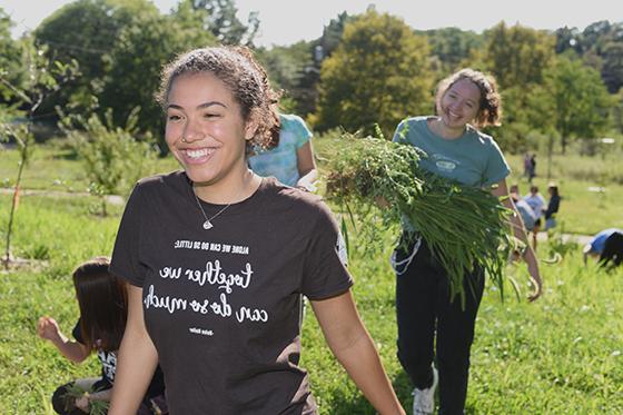 Photo of smiling Chatham University students working at Eden Hall Farm in the field removing weeds.