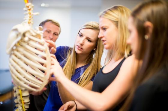 Photo of three students and a professor examining an educational skeleton in Chatham University lab. 