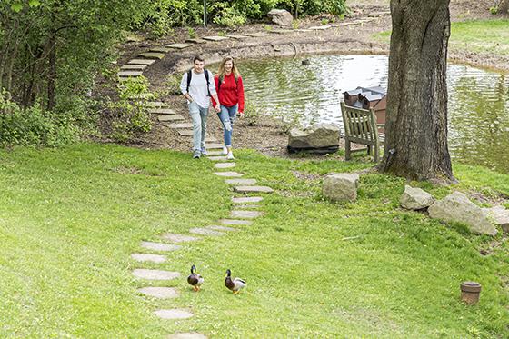 两名波胆网站的学生手牵手沿着荫边校园池塘周围的小路散步. 