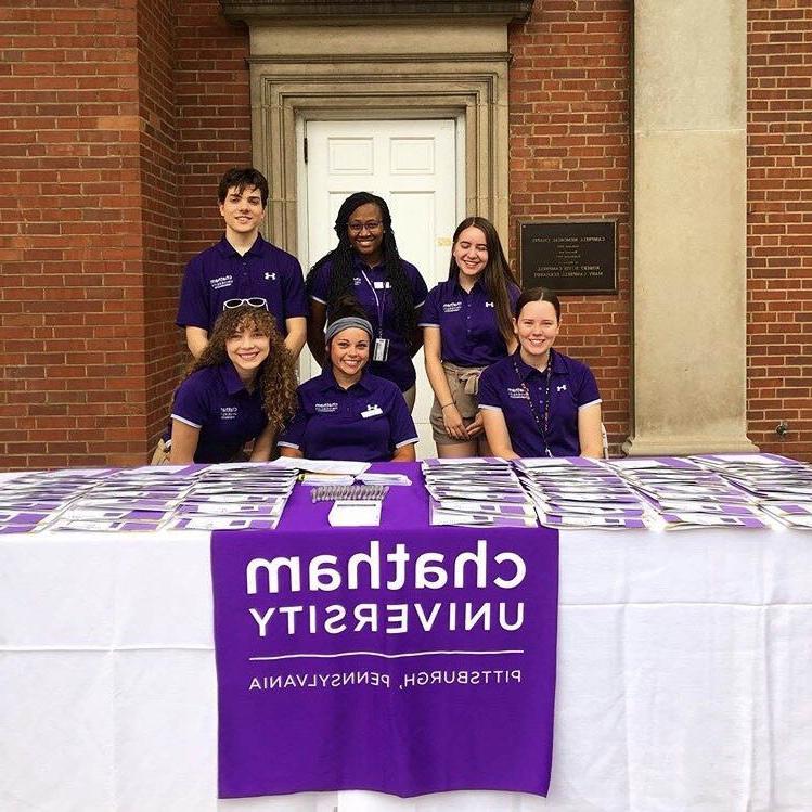 图为六名身穿紫色衬衫的波胆网站学生, 在足球波胆平台外面的桌子上工作