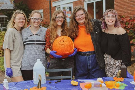 Photo of Chatham University students posing with a pumpkin, wearing science goggles