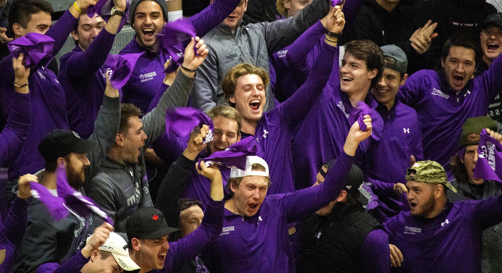 Photo of a group of Chatham University students wearing purple, cheering in a student section at a sporting event. 